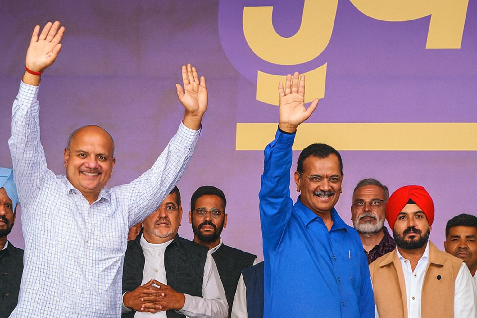 Outdoor rally scene, leaders smiling and waving, large Hindi banner visible, group of supporters in varied attire.